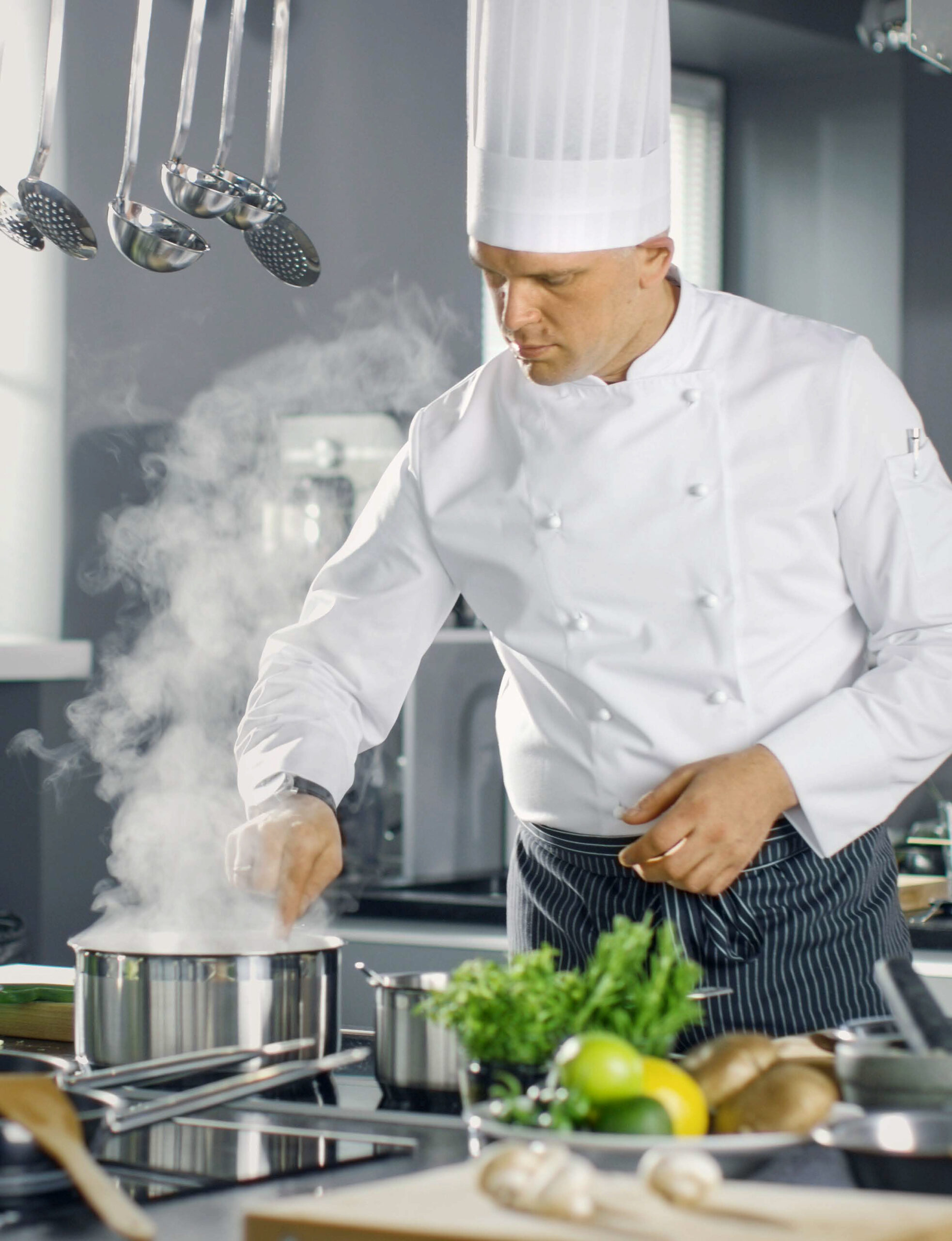 Um homem com roupas brancas de cozinheiro mexendo panelas e frigideiras